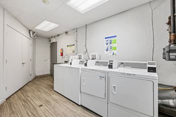 A clean, white-walled industrial laundry room with a row of washers and dryers.